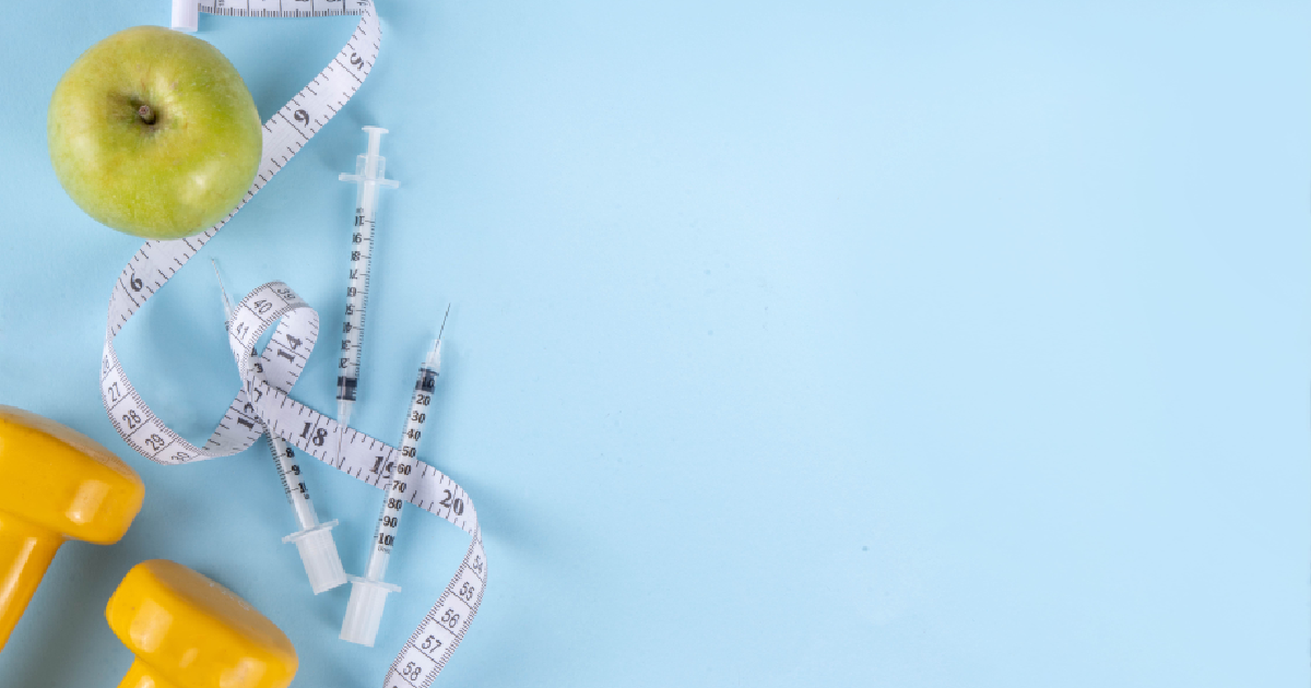 Weight loss concept with syringes, measuring tape, apple, and yellow dumbbells on a blue background, representing Weight Loss Injections in Madison, WI.
